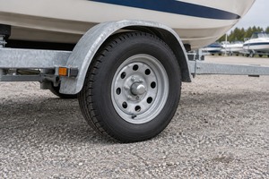 Boat trailer tire and galvanized steel wheel beneath a metal fender and white boat hull.