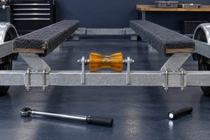 Empty galvanized boat trailer with carpeted bunk boards and an orange keel roller, a torque wrench and flashlight on the shop floor.