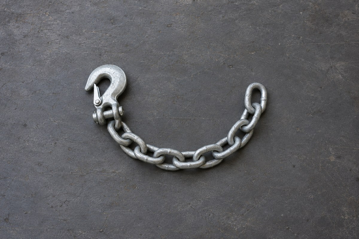 Short length of galvanized trailer safety chain with a latched clevis hook, lying on a dark shop floor.